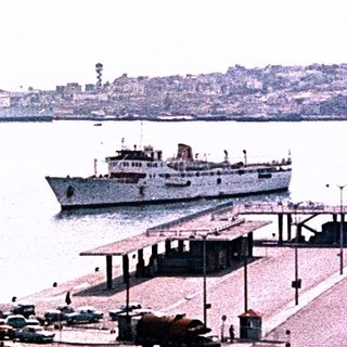 Historic port city with vintage ferry, trams, and waterfront buildings.