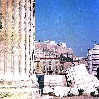 Ancient Greek ruins with Acropolis in background.