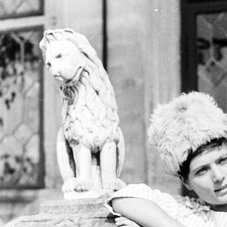 Elegant woman posing beside a stone lion statue.