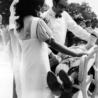 Two people adjusting a man's tie outdoors.