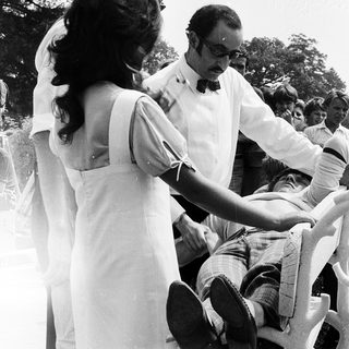 Two people adjusting a man's tie outdoors.