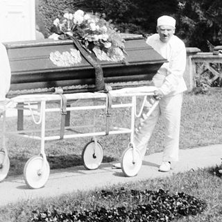Funeral procession with casket being carried outdoors.
