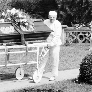 Funeral procession with casket being carried outdoors.