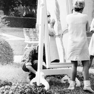 Three women examining a large mirror outdoors.