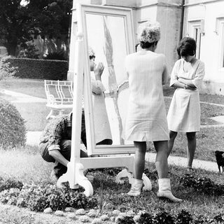 Three women examining a large mirror outdoors.