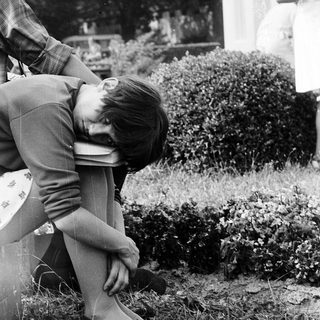 A man kneeling in grass, adjusting a camera.