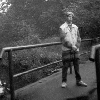 Person standing on a bridge in a forested area.
