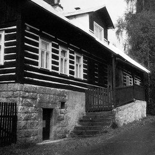 Rustic wooden house with stone foundation on a rural road.