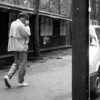 Street scene with people using old-style phones near parked cars.