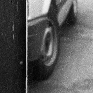 Street scene with people using old-style phones near parked cars.