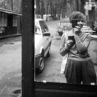 Street scene with people using old-style phones near parked cars.