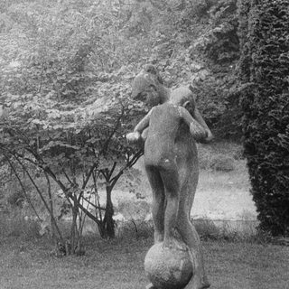 Statue of a person holding a ball in park setting.