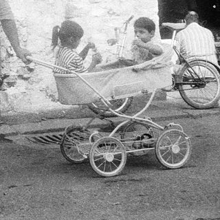 Street scene with man pushing baby stroller past crates.