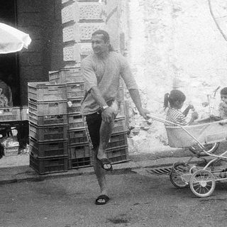 Street scene with man pushing baby stroller past crates.