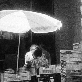 Street scene with man pushing baby stroller past crates.