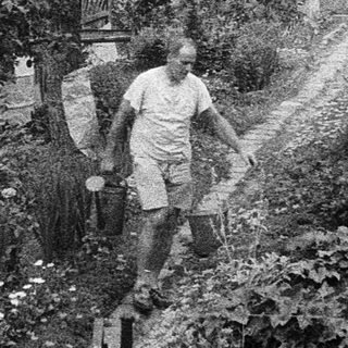 People gardening on a sloped, overgrown hillside.