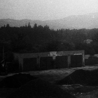 Rural landscape with garage, forest, and distant mountains.