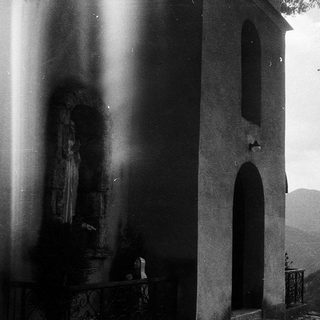 Small rural chapel with statue, mountain backdrop.