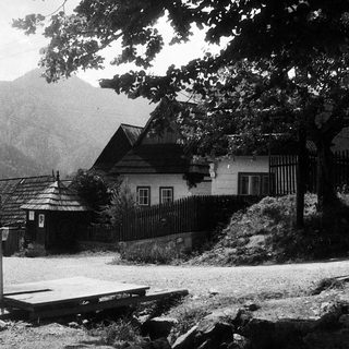 Rural house with wooden architecture, surrounded by trees and mountains.