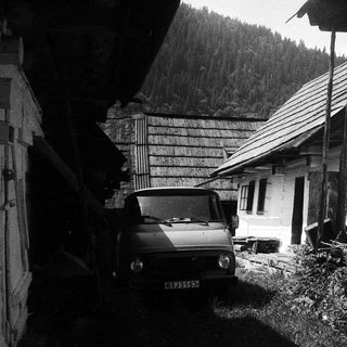 Rural house with vintage car parked beside rustic buildings.