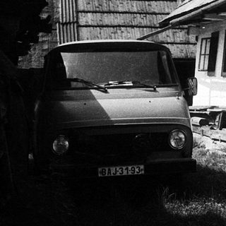 Rural house with vintage car parked beside rustic buildings.