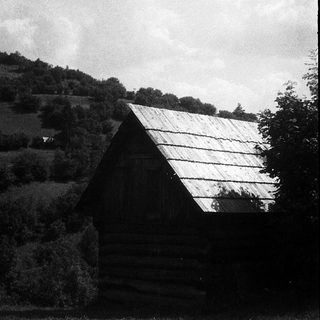 Rural wooden house with sloped roof, surrounded by fields and trees.