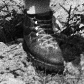 Old man examining rocks in rugged outdoor terrain.