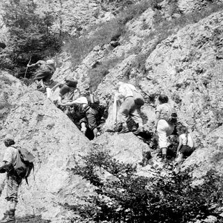 Soldiers climbing rugged mountain terrain.