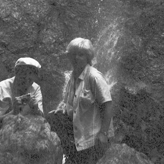 Two people standing near a powerful waterfall.