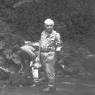 Two men and a dog in a river, likely searching for or handling fish.
