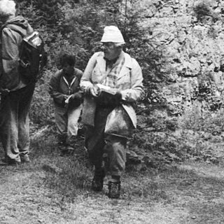 Three hikers resting on forest trail near rock formation.