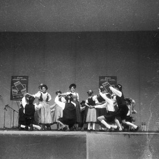 Group performing dance routine on stage with live band.
