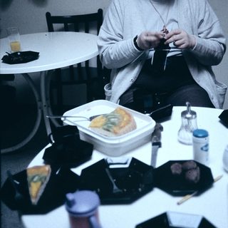 Person eating lunch while crocheting indoors.