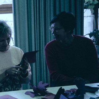Three people crafting together indoors with paper.
