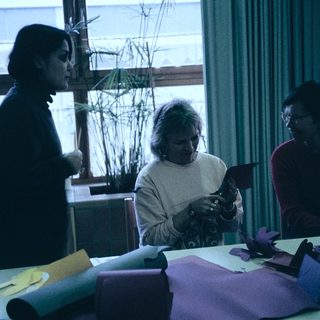 Three people crafting together indoors with paper.