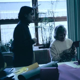 Three people crafting together indoors with paper.
