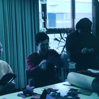 Three people crafting together indoors with paper.