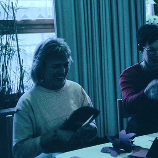 Three people crafting together indoors with paper.