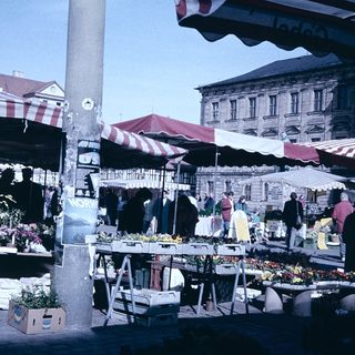 Outdoor market with flower stalls and shoppers.