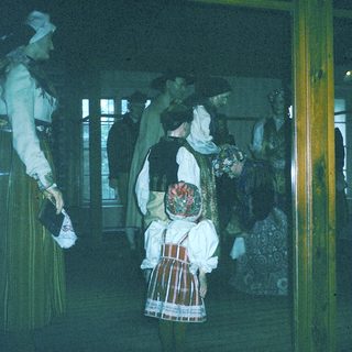 Traditional folk costumes in a dimly lit indoor gathering.