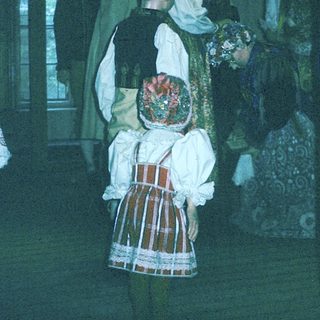 Traditional folk costumes in a dimly lit indoor gathering.