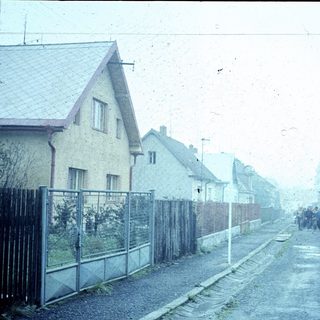 Suburban street with houses, fence, and people walking.