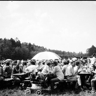 Outdoor gathering with people seated at tables under umbrellas.