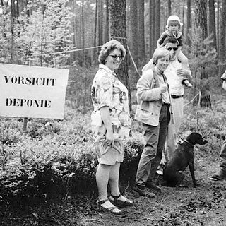 Family hiking with warning sign "Vorsicht Deponie" in forest.