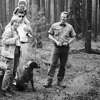Family hiking with warning sign "Vorsicht Deponie" in forest.