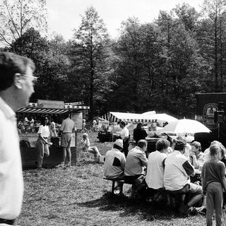 Outdoor concert or event with crowd seated on benches.