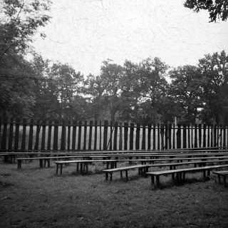 Empty outdoor seating area with wooden benches and fenced background.