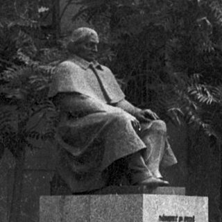 Statue of seated historical figure in park setting.