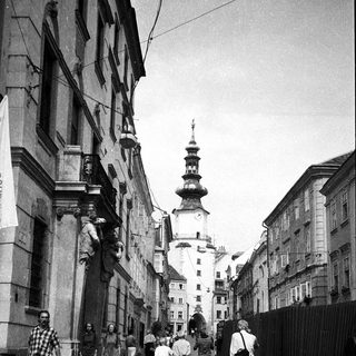 Historic European street with people walking, old buildings, and tower in background.