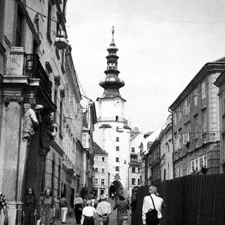 Historic European street with people walking, old buildings, and tower in background.